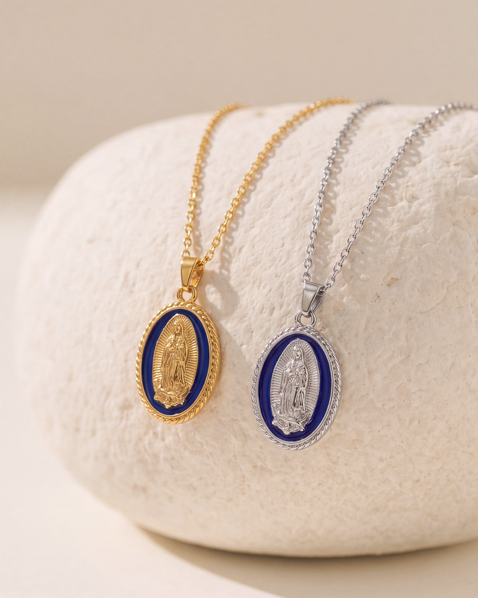 Collares dorado y plateado de la Virgen María con medallones ovalados de esmalte azul sobre superficie de piedra clara
