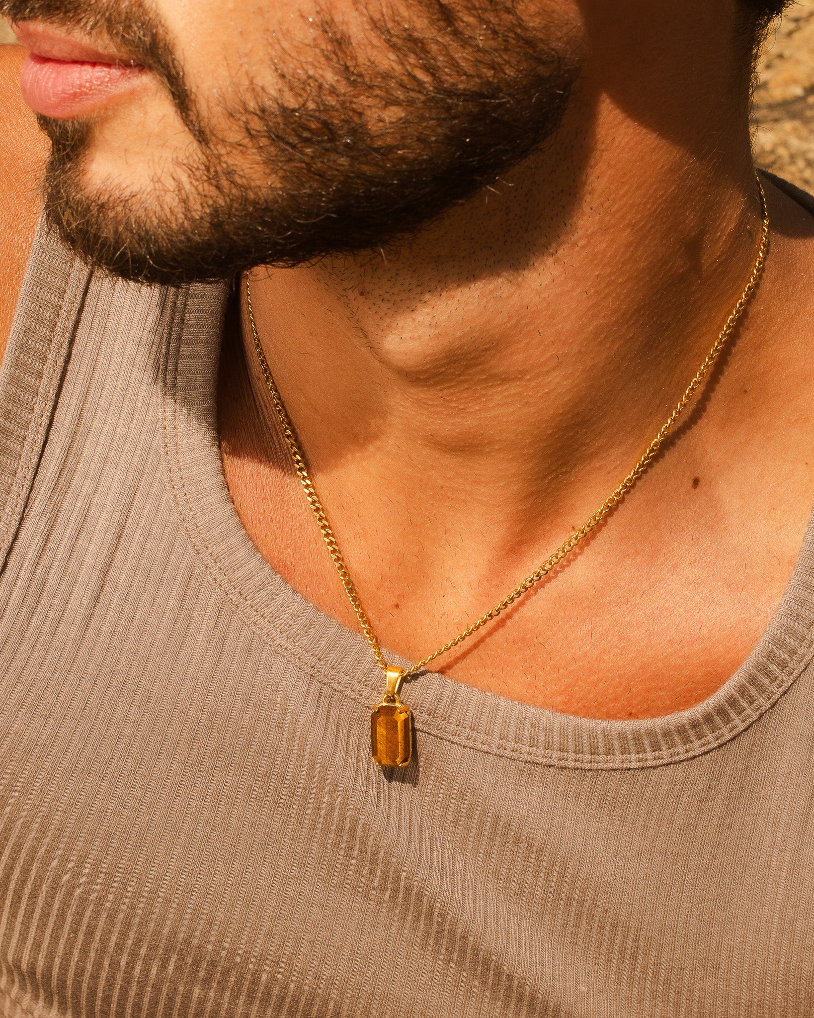 Collar de cadena dorada con gran colgante rectangular ámbar sobre un pecho iluminado por el sol.