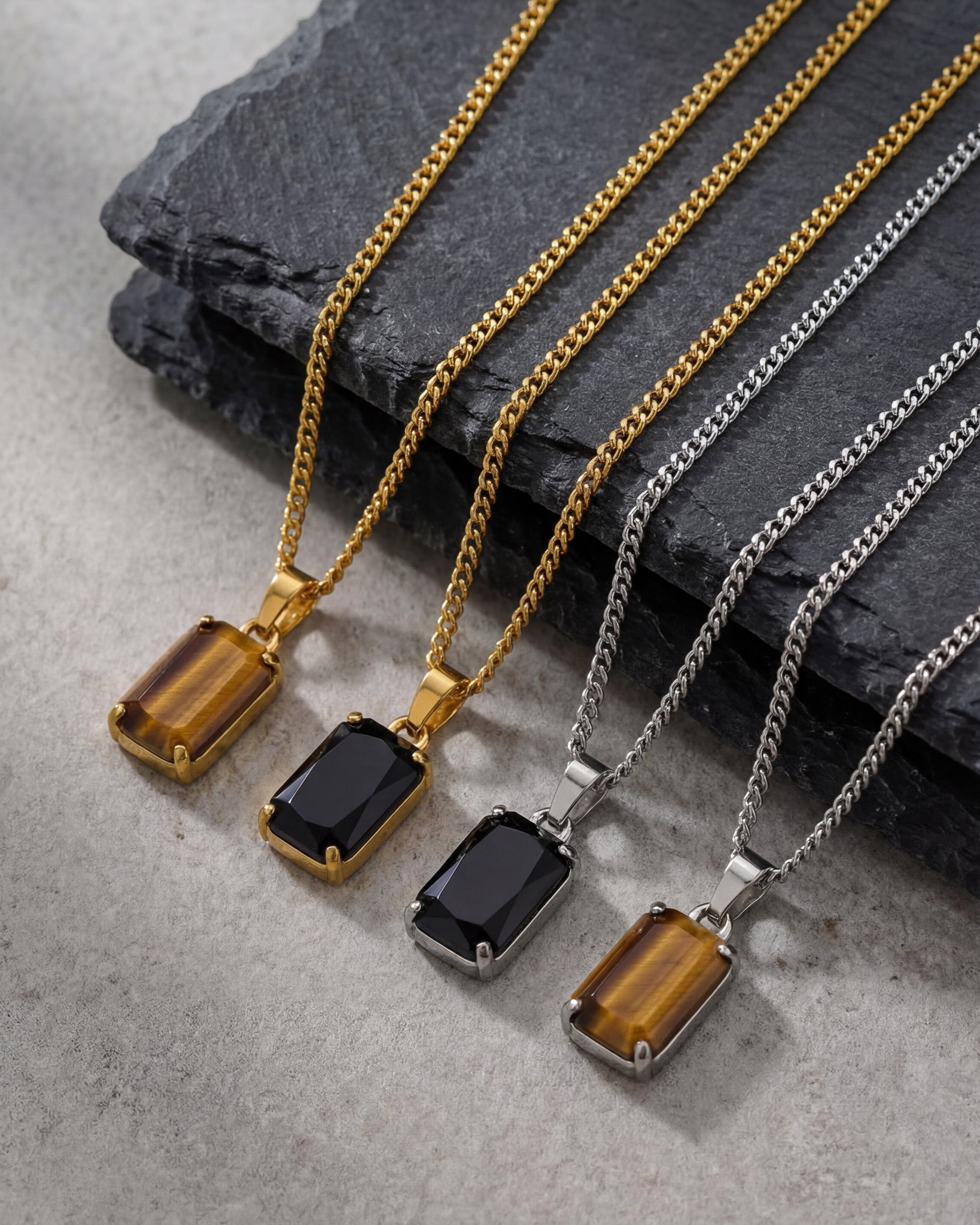 Rows of VOLT necklaces in gold and silver finishes with rectangular black stone pendants on a dark backdrop