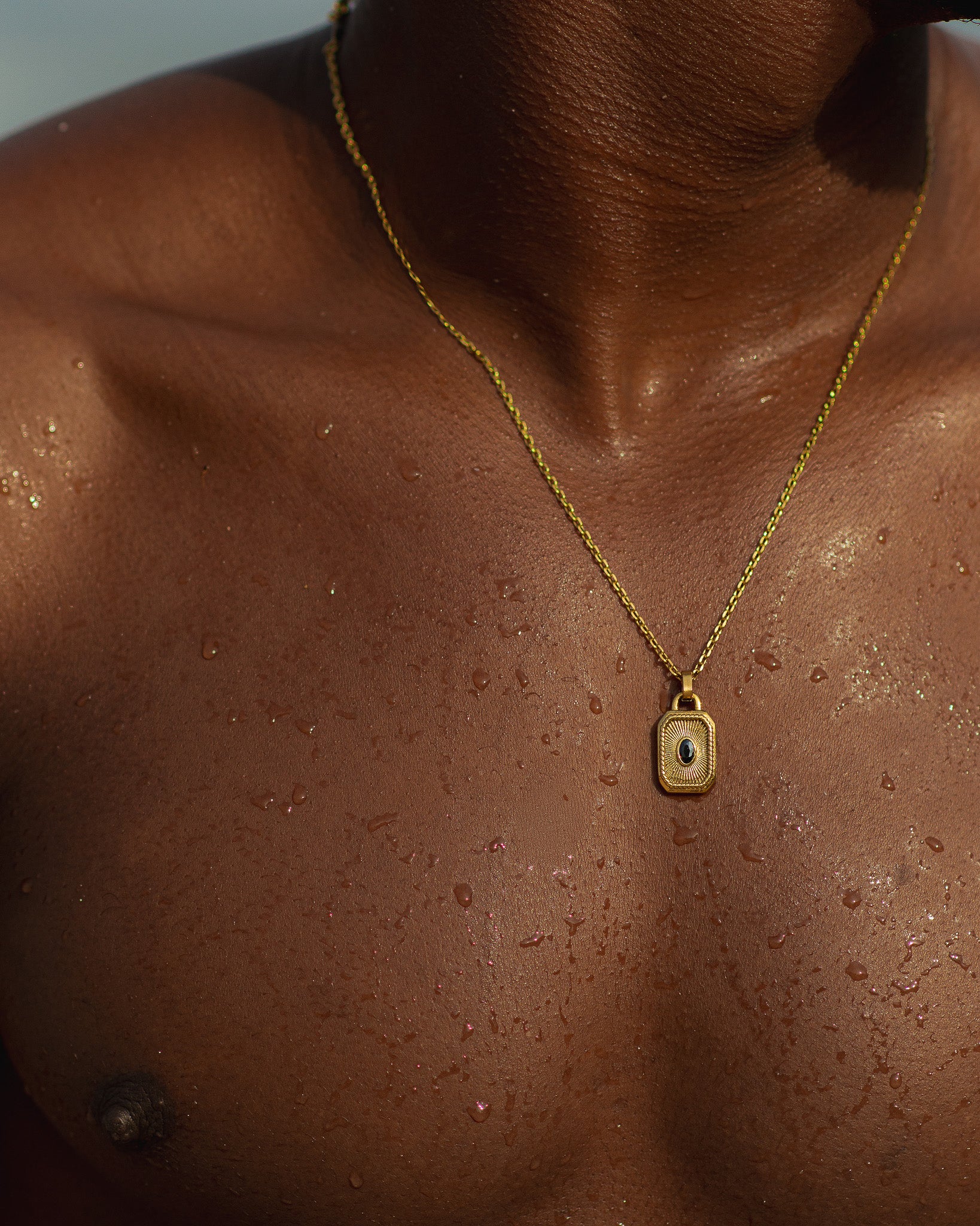 Gold necklace with a rectangular pendant and blue gemstone resting on a model's chest