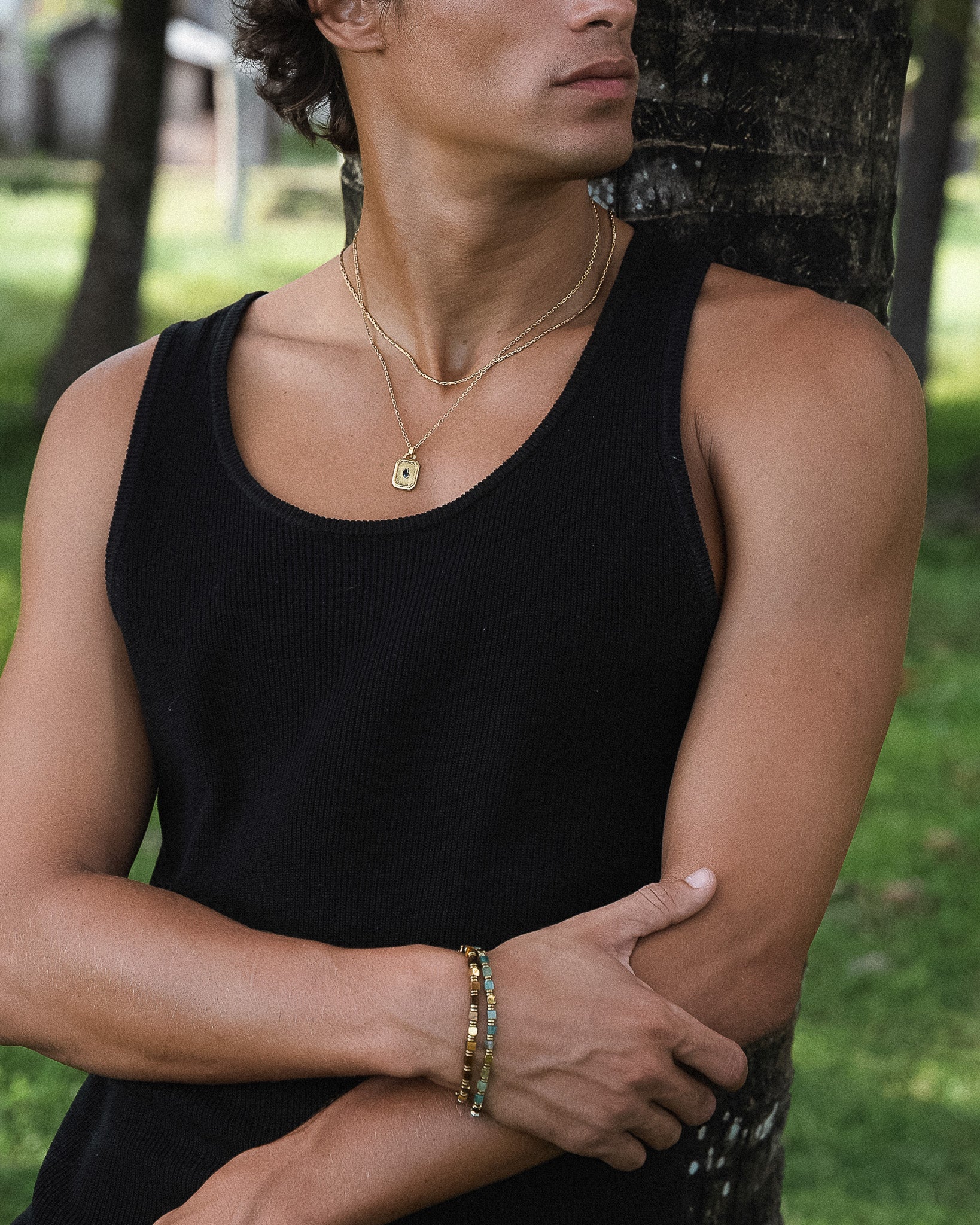 Gold rectangular pendant with blue gemstone on a two strand necklace worn over a black tank top