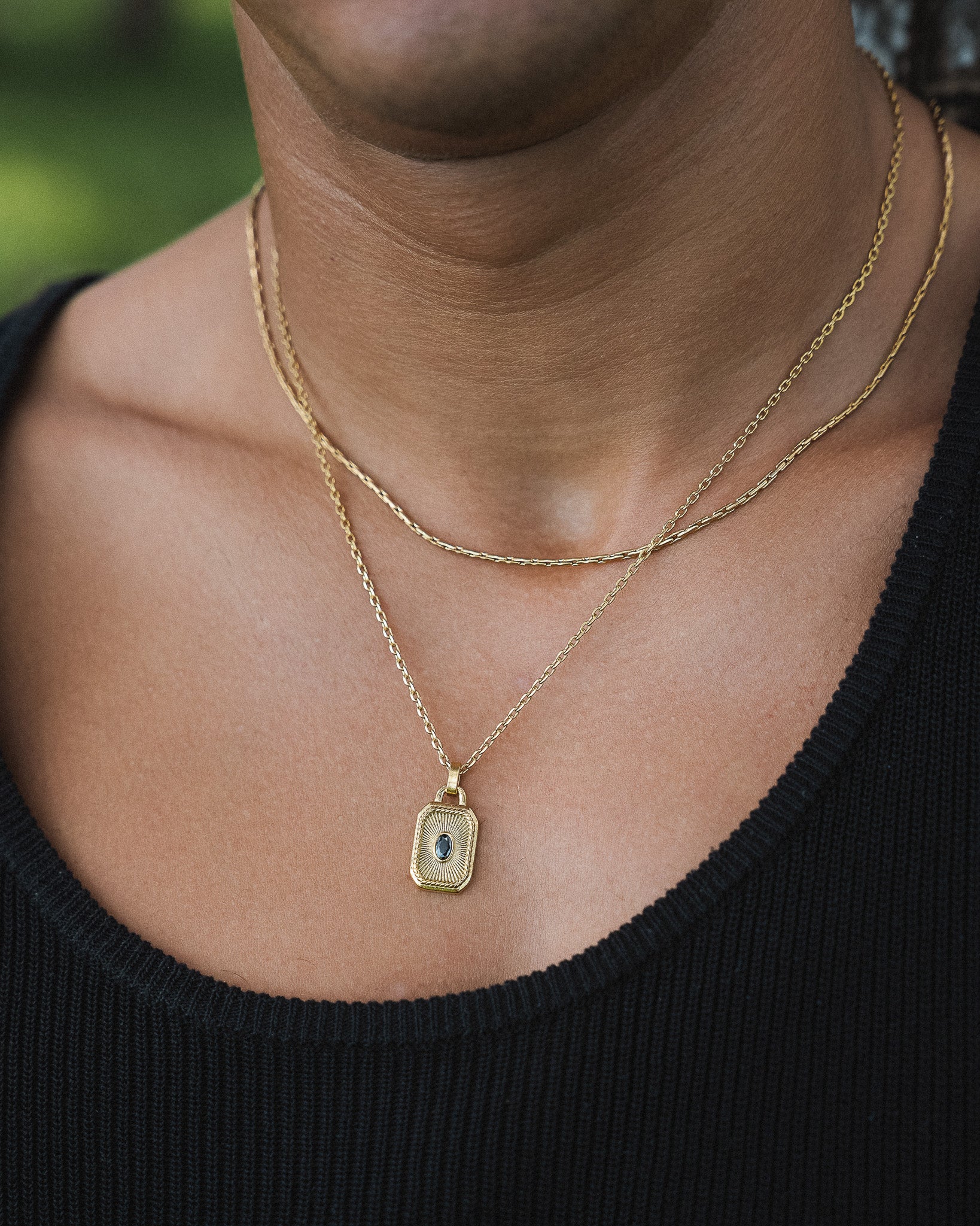 Two layered gold chain necklaces around the neck on a person wearing a black top
