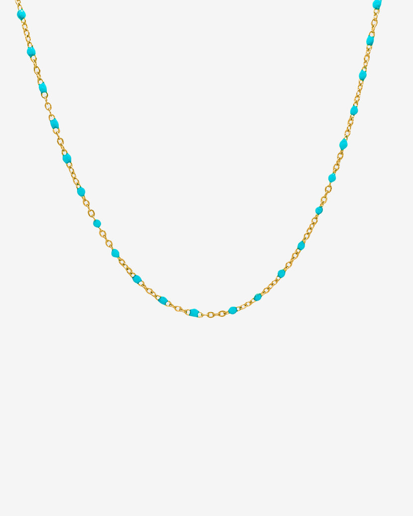 Collar de cadena dorada con cuentas turquesa sobre fondo blanco
