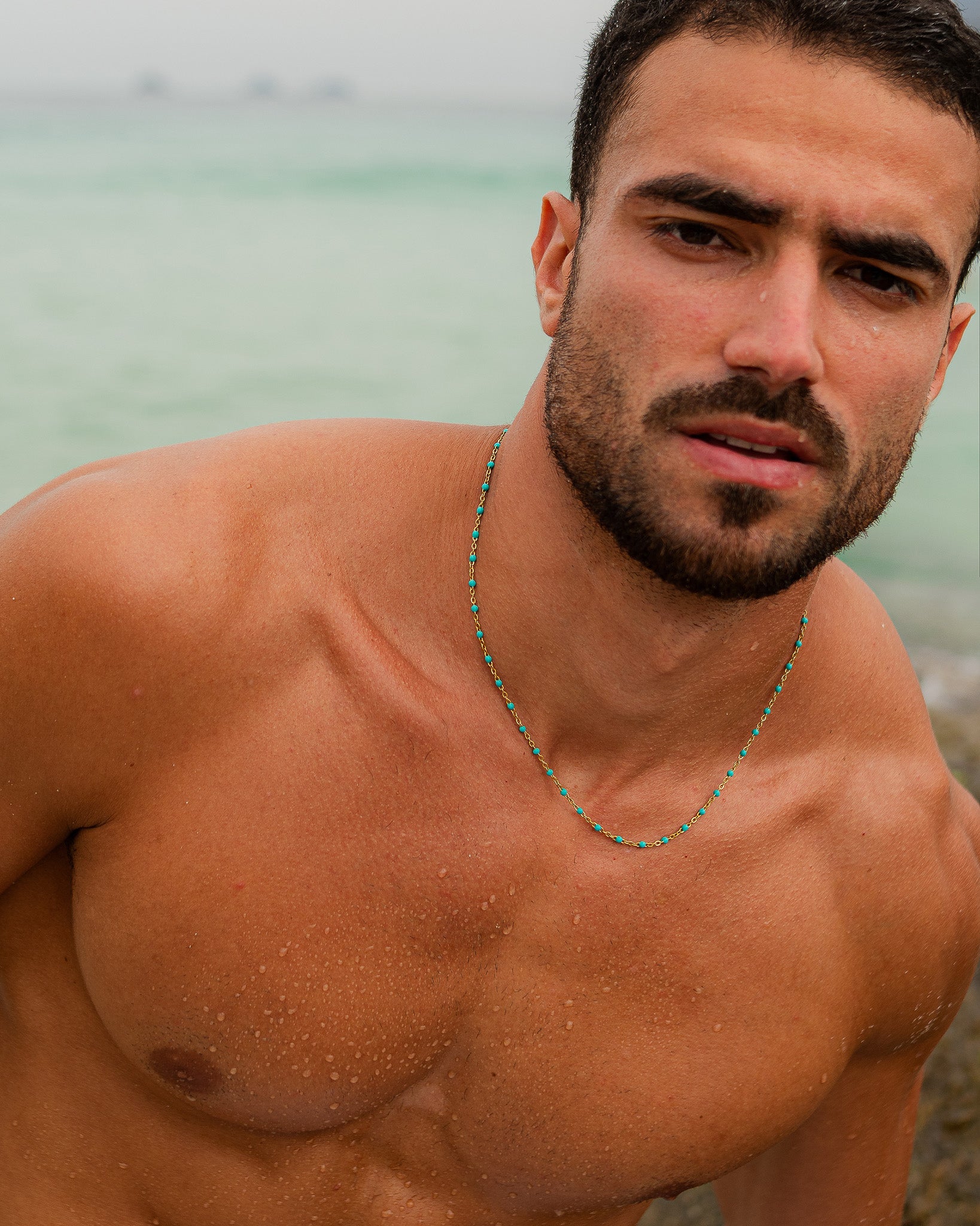 Portrait of a man at the beach wearing a turquoise bead gold chain