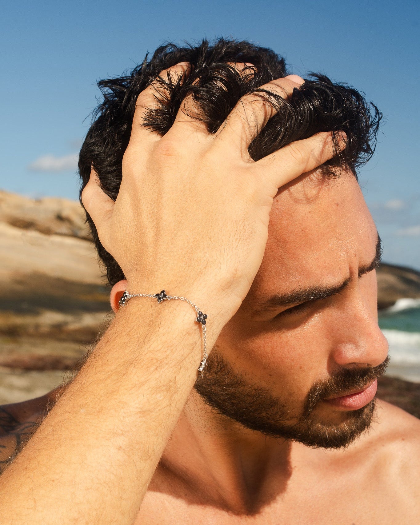 Silver Clover bracelet with black gemstone clover charms worn on a man's wrist outdoors by the coast.