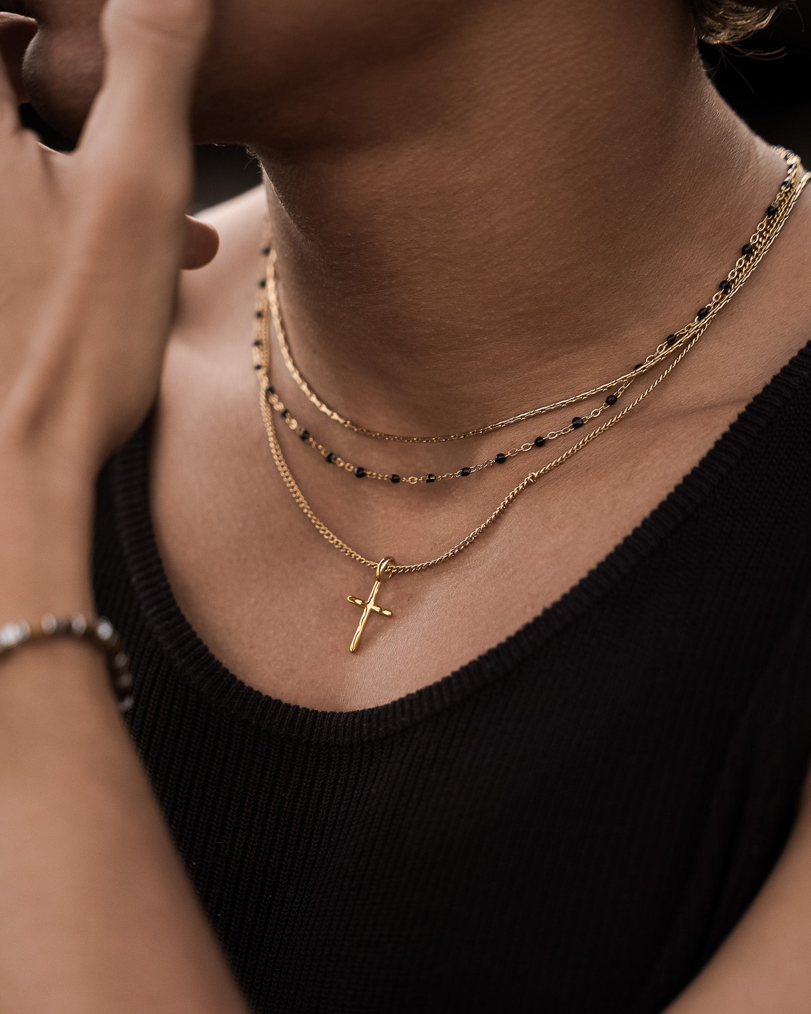 Profile of a model wearing layered gold necklaces including a cross pendant