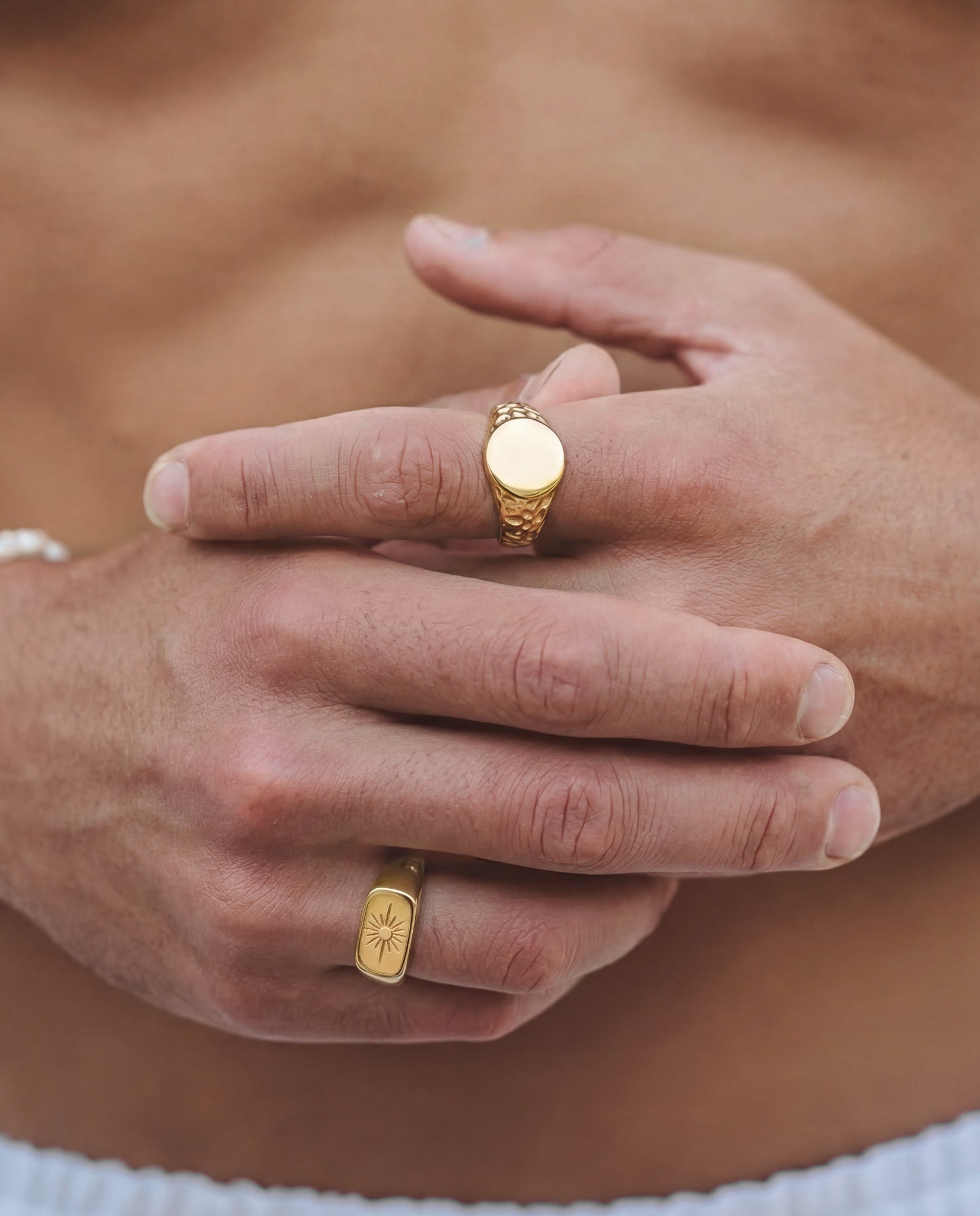 Eden gold ring with a smooth round face and textured patterned band worn on the finger