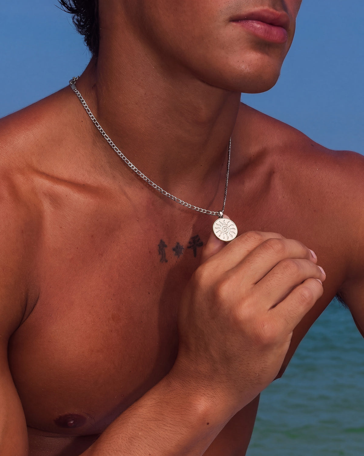 Portrait of a person wearing energy silver necklace with sunburst pendant resting on the collarbone.