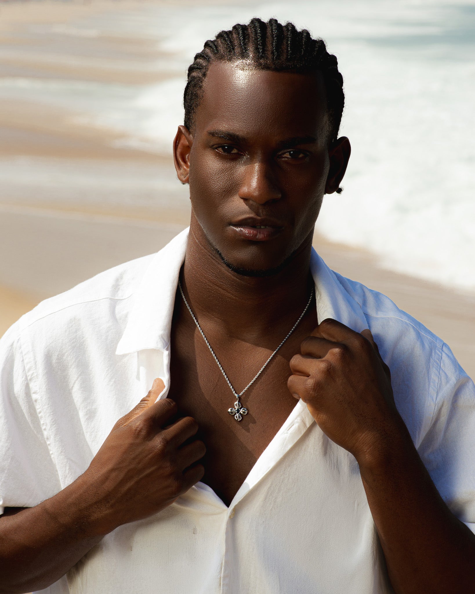 FLARE SILVER NECKLACE with a floral quatrefoil pendant on a model wearing a white shirt at the beach
