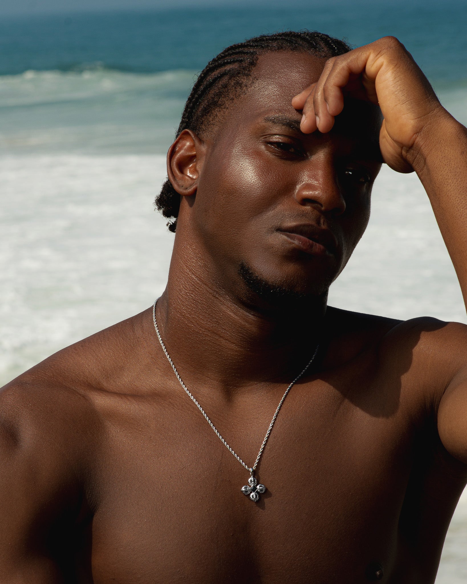 Silver flare necklace with a flower shaped pendant worn by a model at the beach.