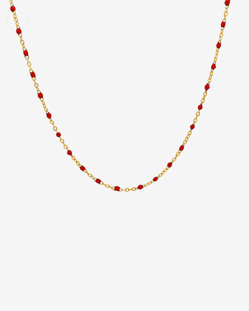 Delicado collar de cadena dorada con cuentas rojas espaciadas uniformemente sobre fondo blanco