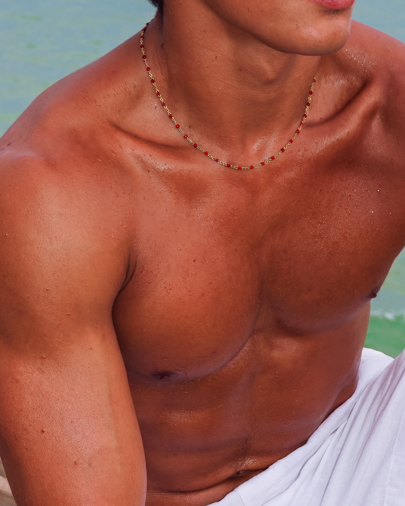 Delicate gold chain necklace with evenly spaced red beads worn around the neck.