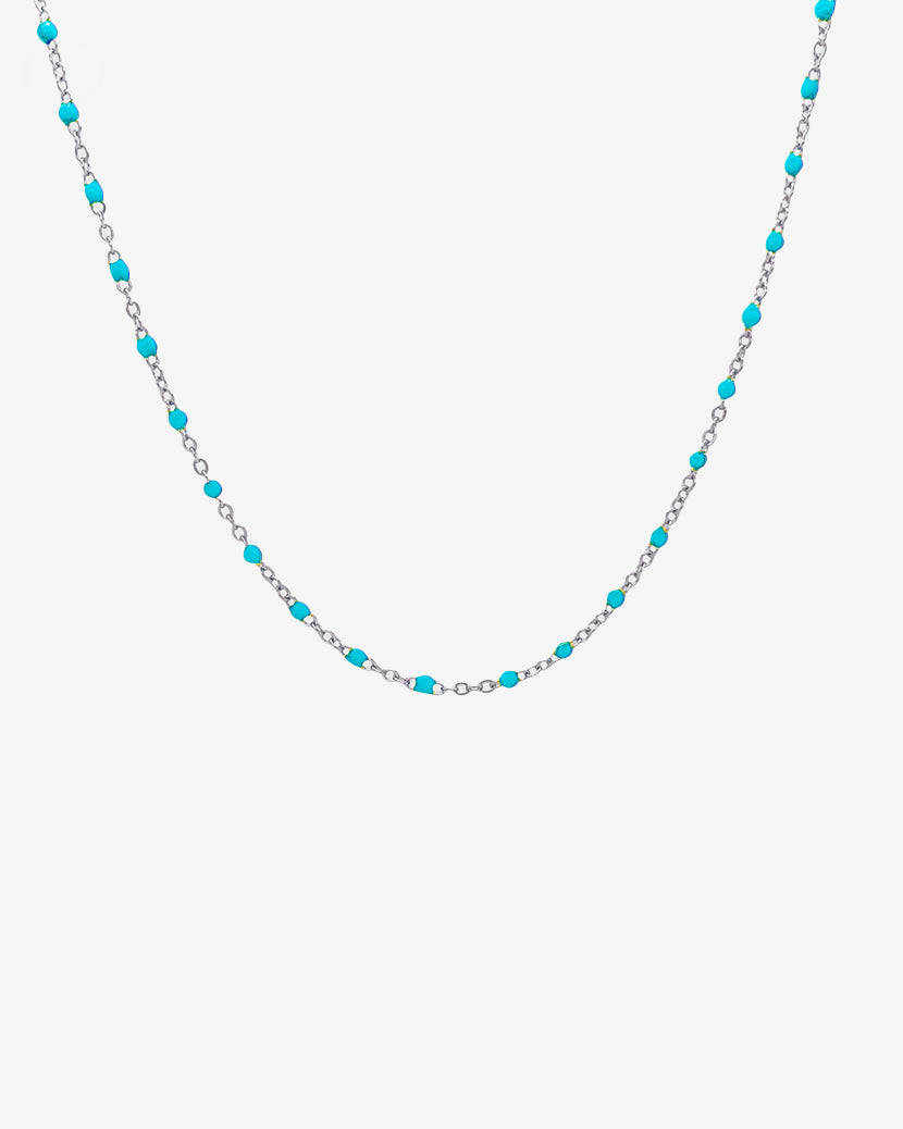 Collar de cadena plateada con cuentas turquesa espaciadas entre los eslabones sobre fondo claro