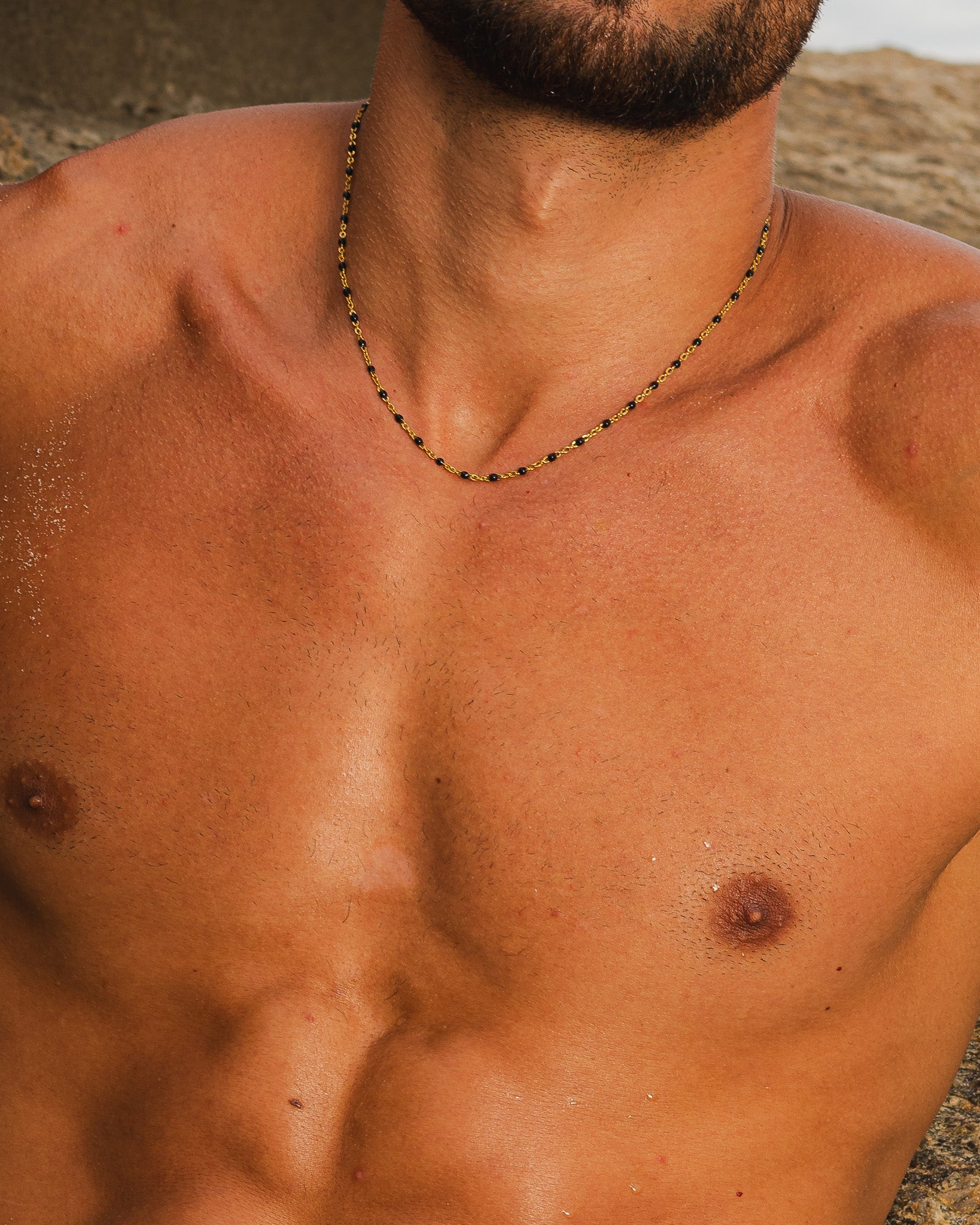 Gold chain with a large rectangular textured pendant resting on the man's chest.