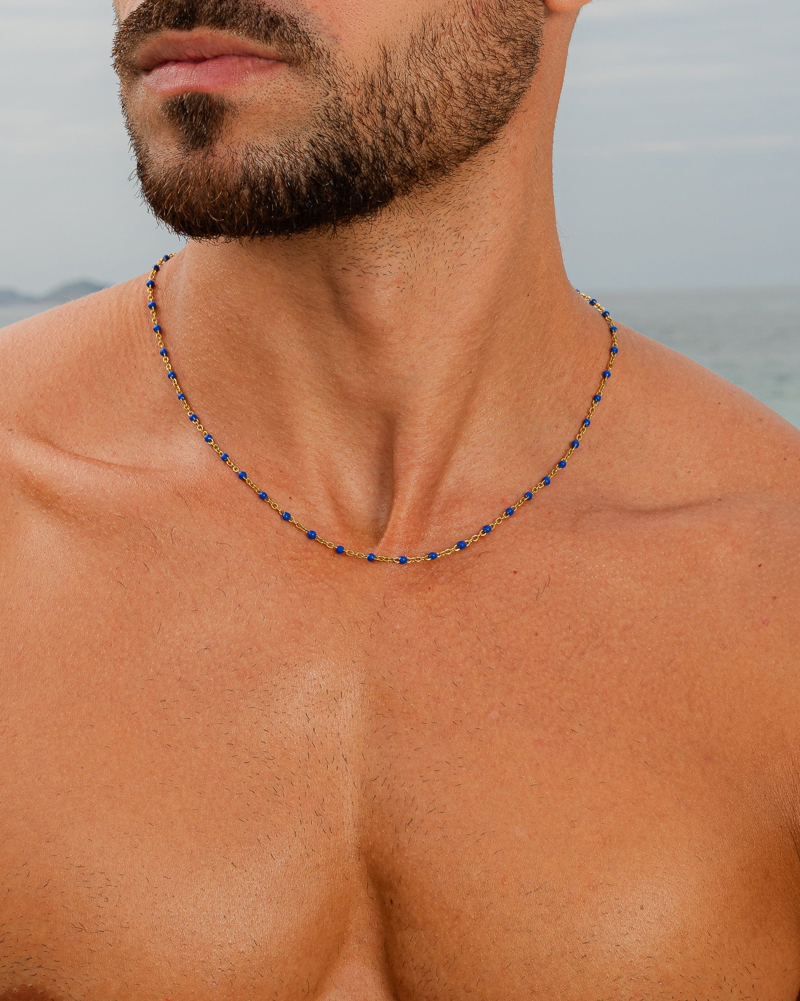 Gold chain with blue beads around a man's neck at the beach.