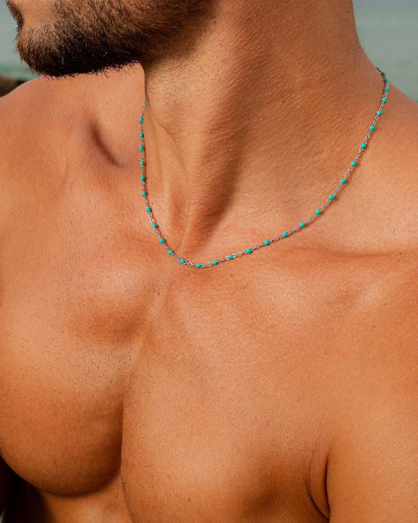 silver chain necklace with turquoise beads resting on a man's neck