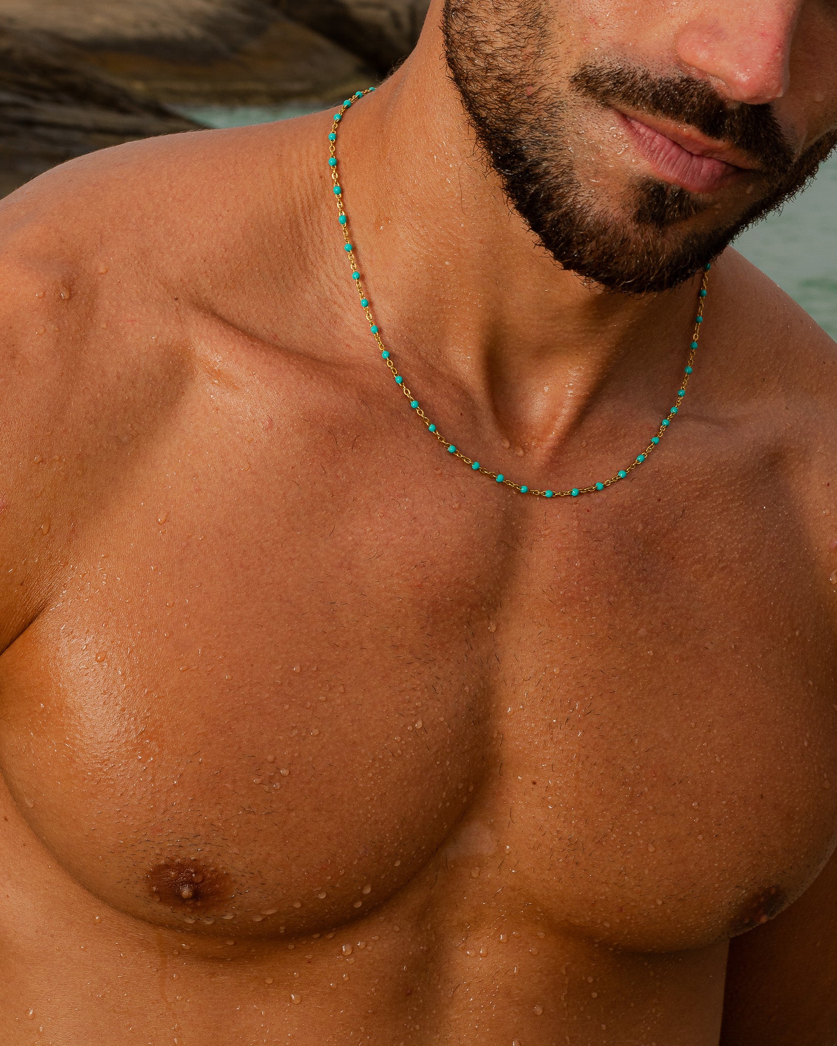 Man wearing a gold chain with turquoise beads and a hanging cross pendant.