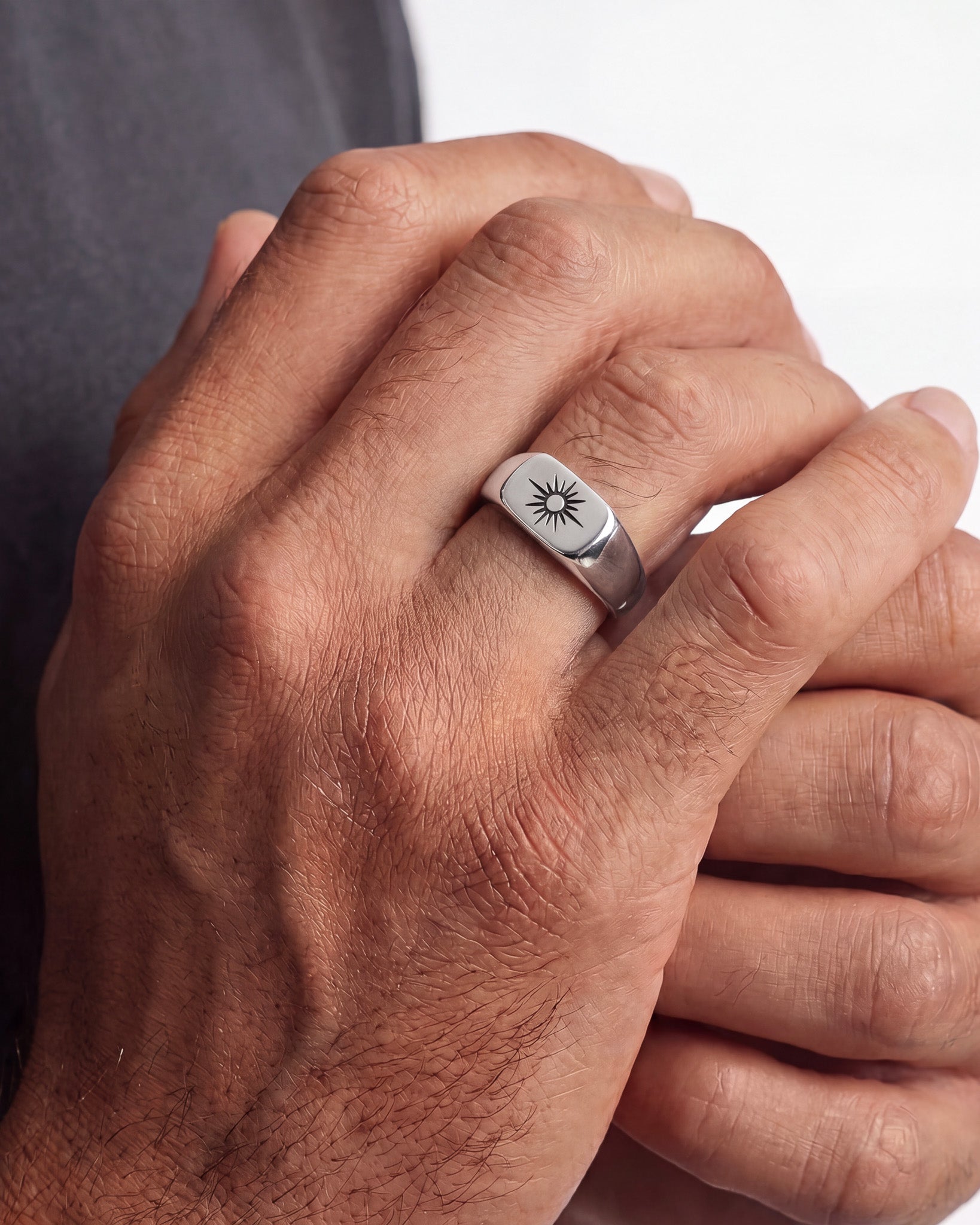 Primer plano de una mano con un anillo sello de plata con diseño de sol radiante.