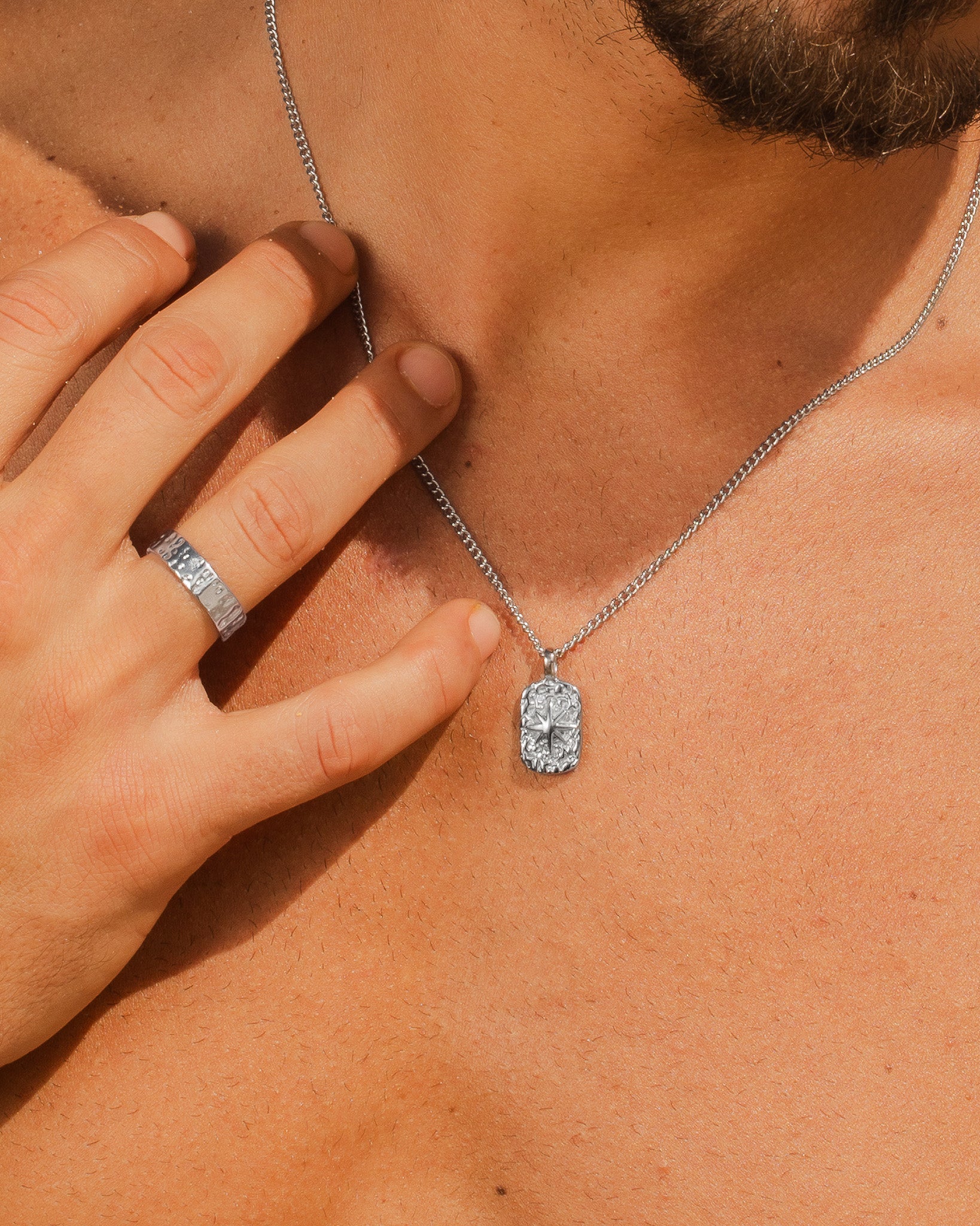 Close-up of a silver IBZ necklace chain resting on a man's neck as he grasps the chain.