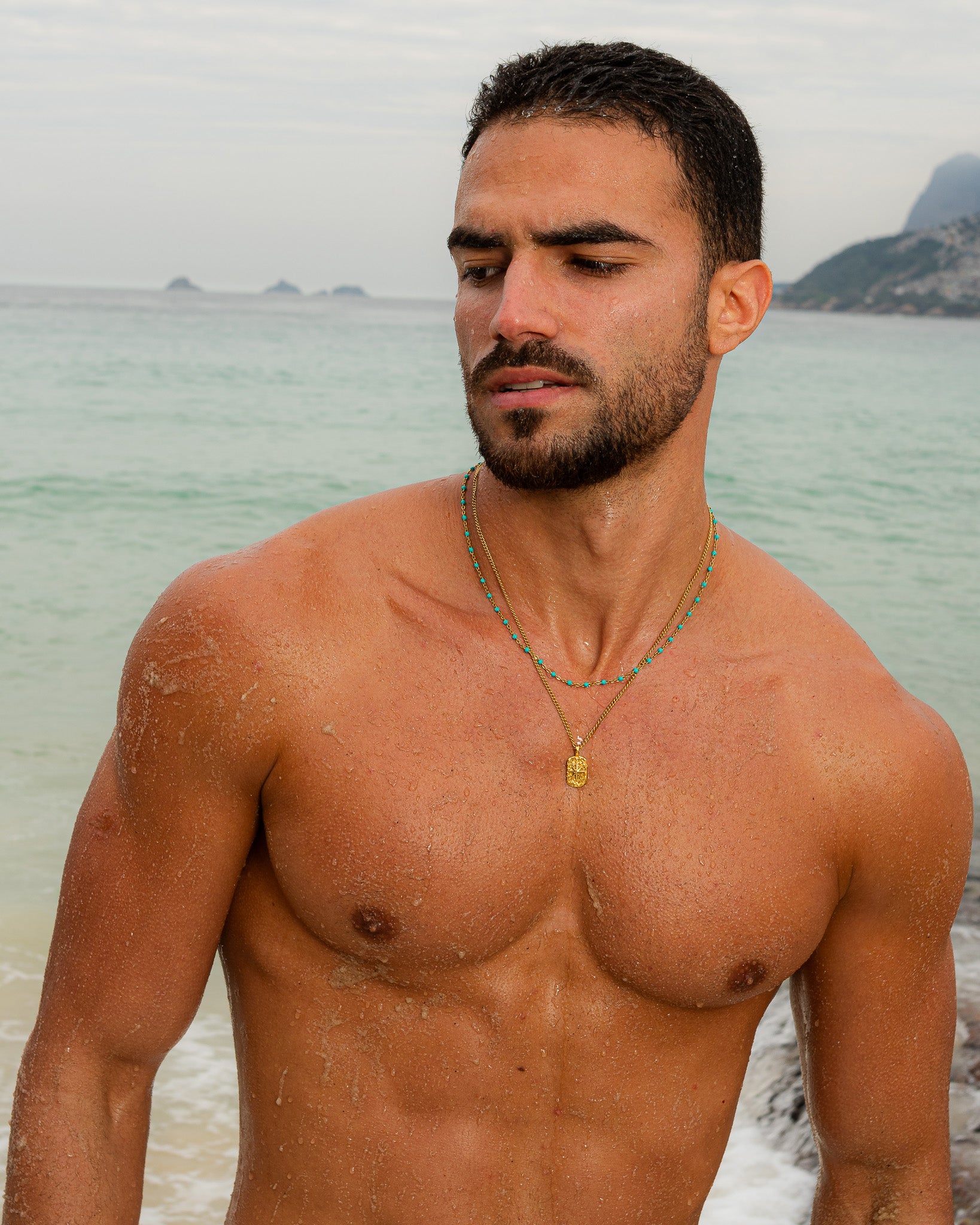 Man at the beach wearing a turquoise bead IBZ Gold Necklace layered with a gold chain