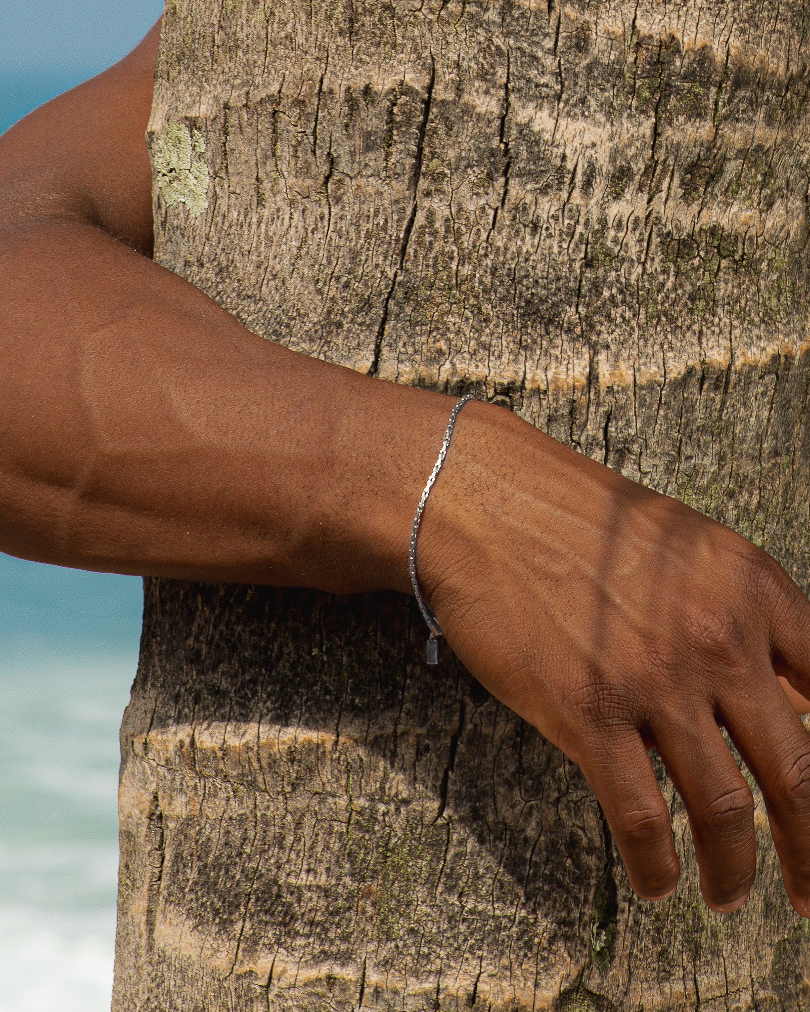 Silver LIRA bracelet on the wrist against a textured tree trunk background