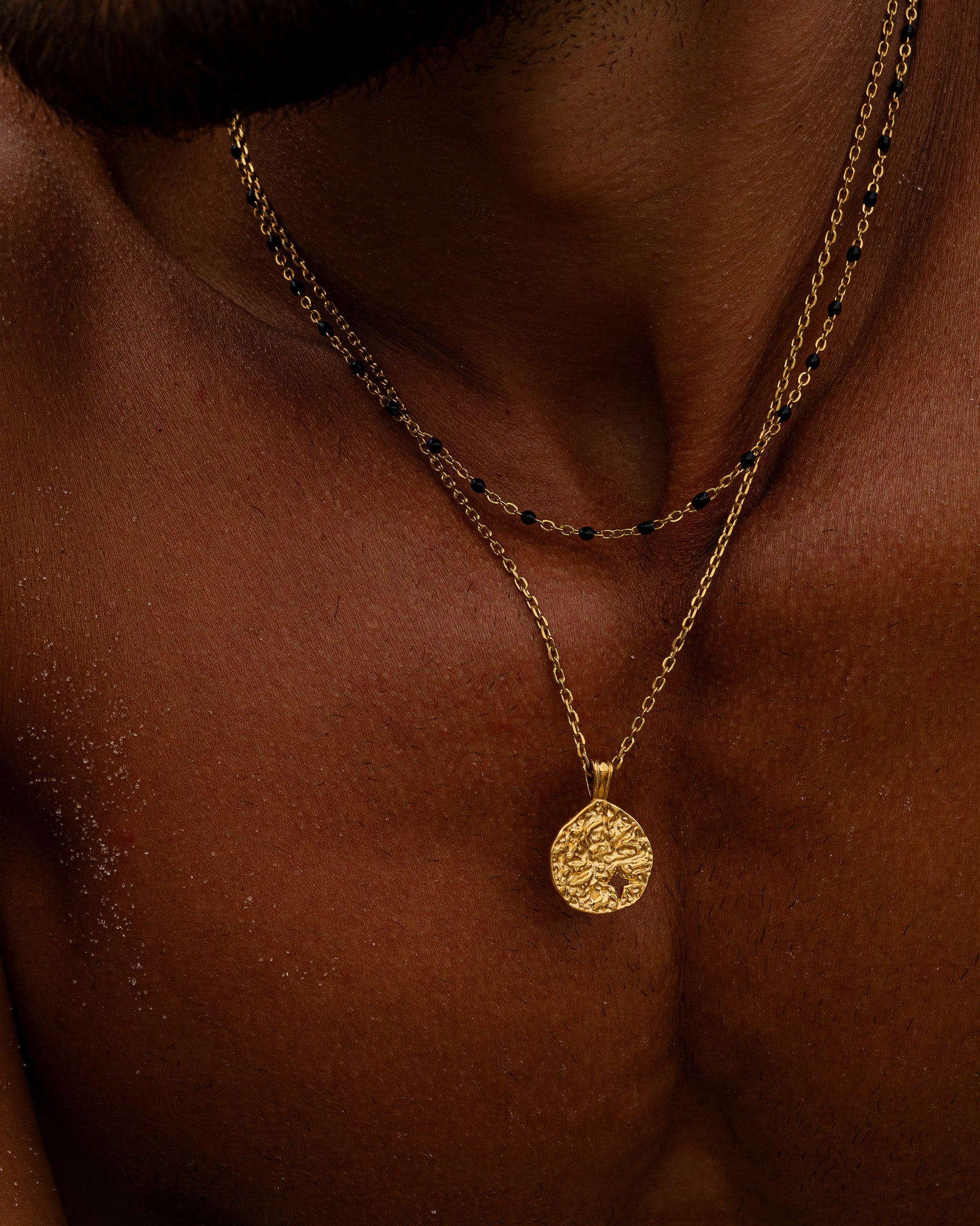 Close up of a gold chain necklace with black bead accents draped around the model’s neck