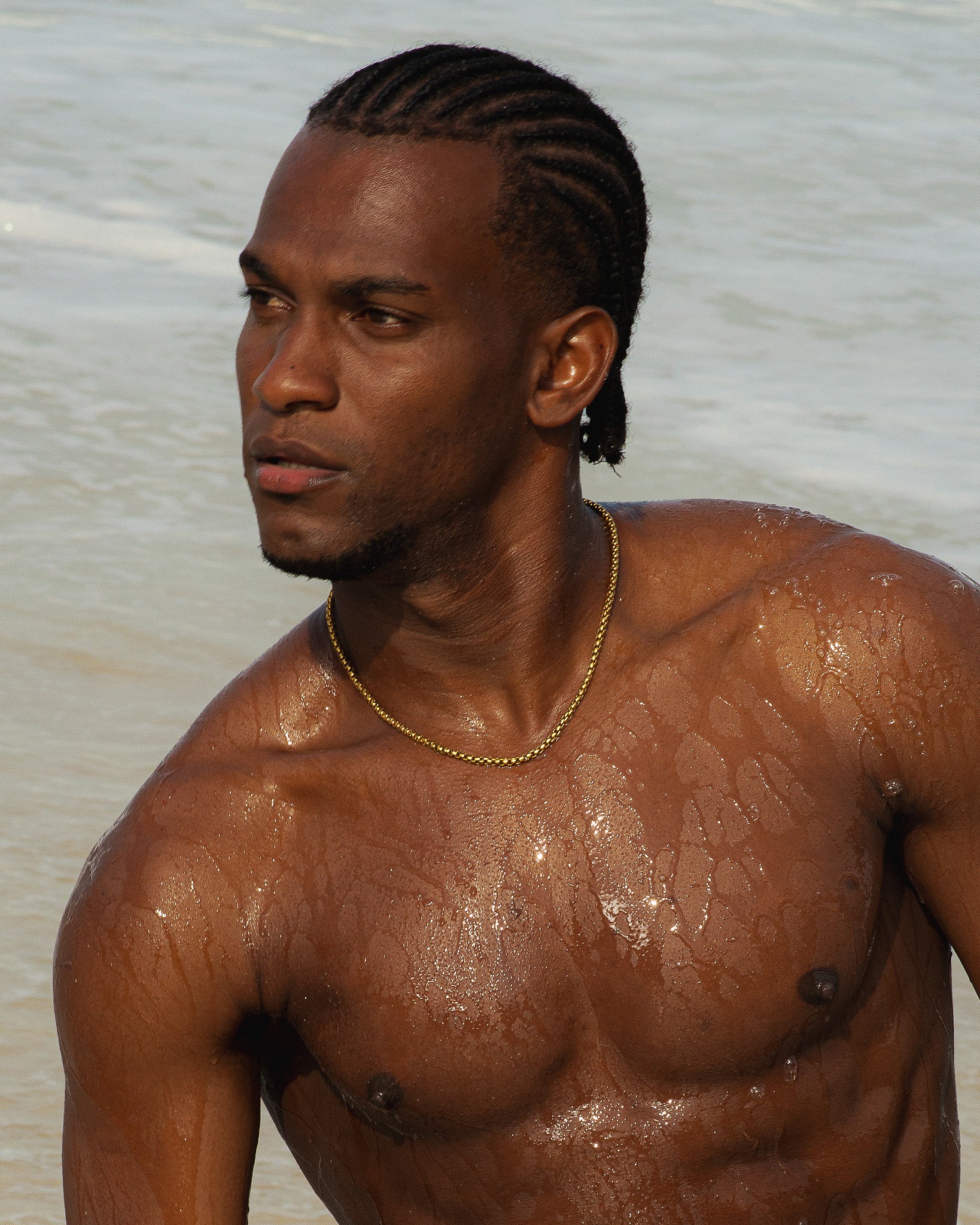NOIR gold chain necklace worn by a shirtless man at the beach