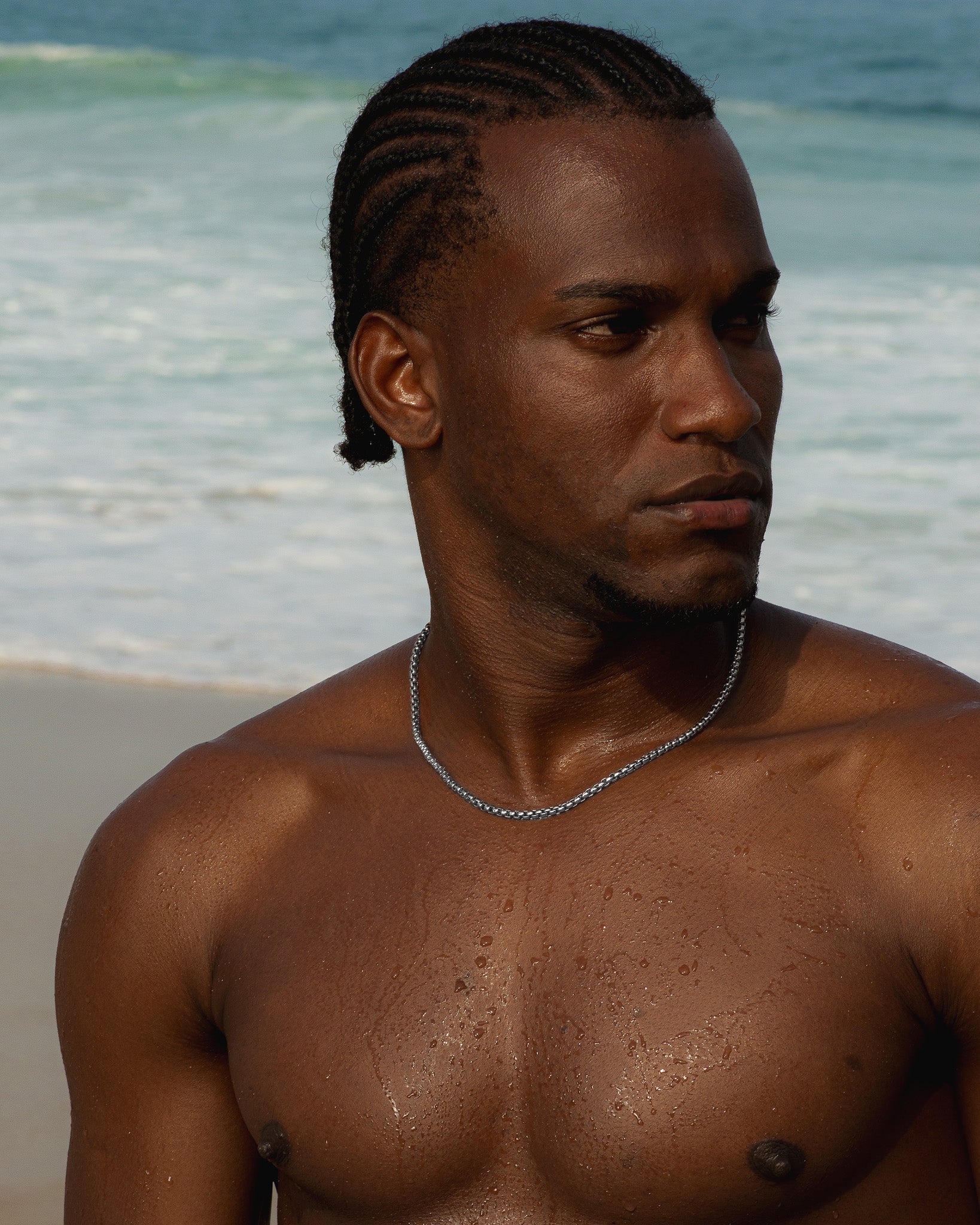 NOIR silver chain necklace worn by a shirtless man at the beach