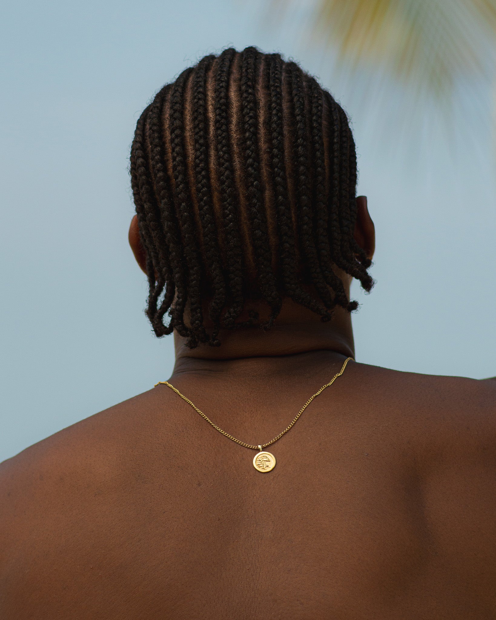 Back of head with cornrow braids and layered gold necklace with black beads around the neck