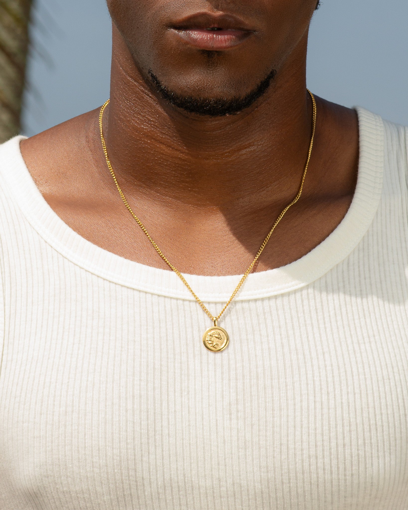 Gold chain necklace with a small round pendant resting on the wearer's chest.