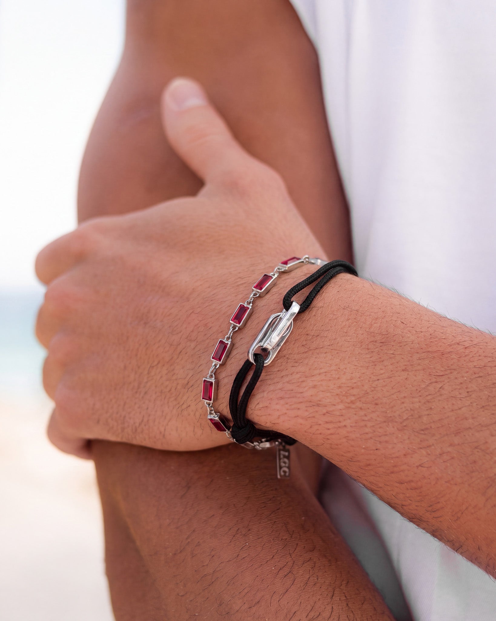Close up of a wrist wearing a red gemstone bracelet paired with a black cord bracelet