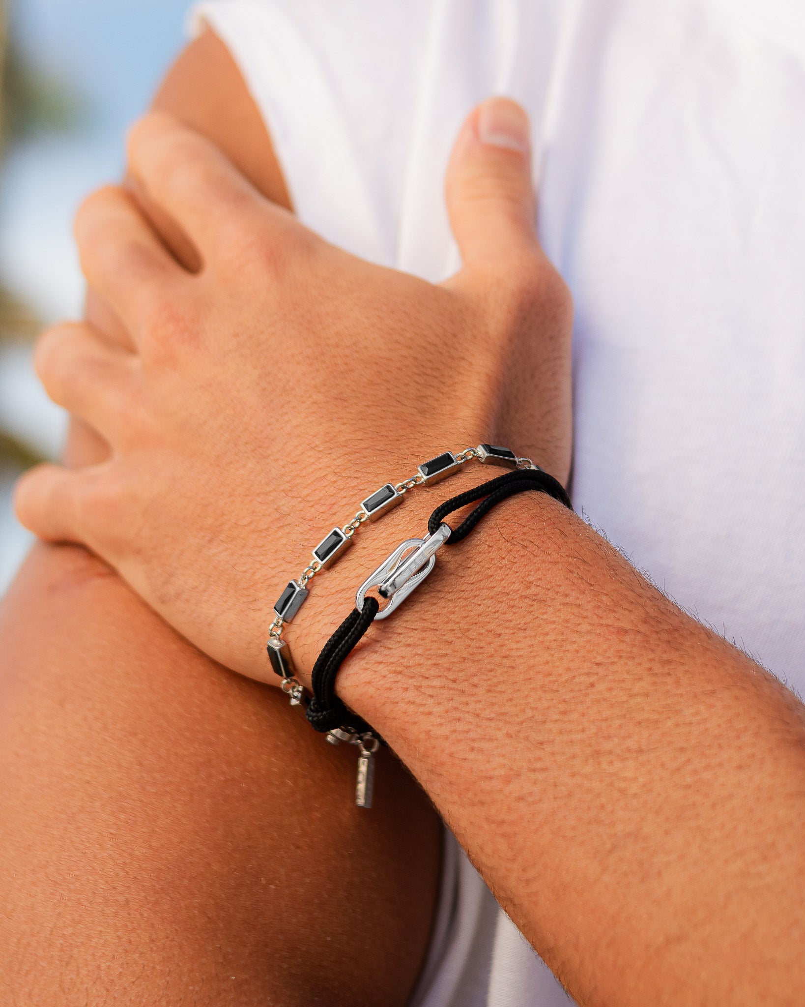 Silver bracelet with black rectangular stones on the wrist paired with a black cord