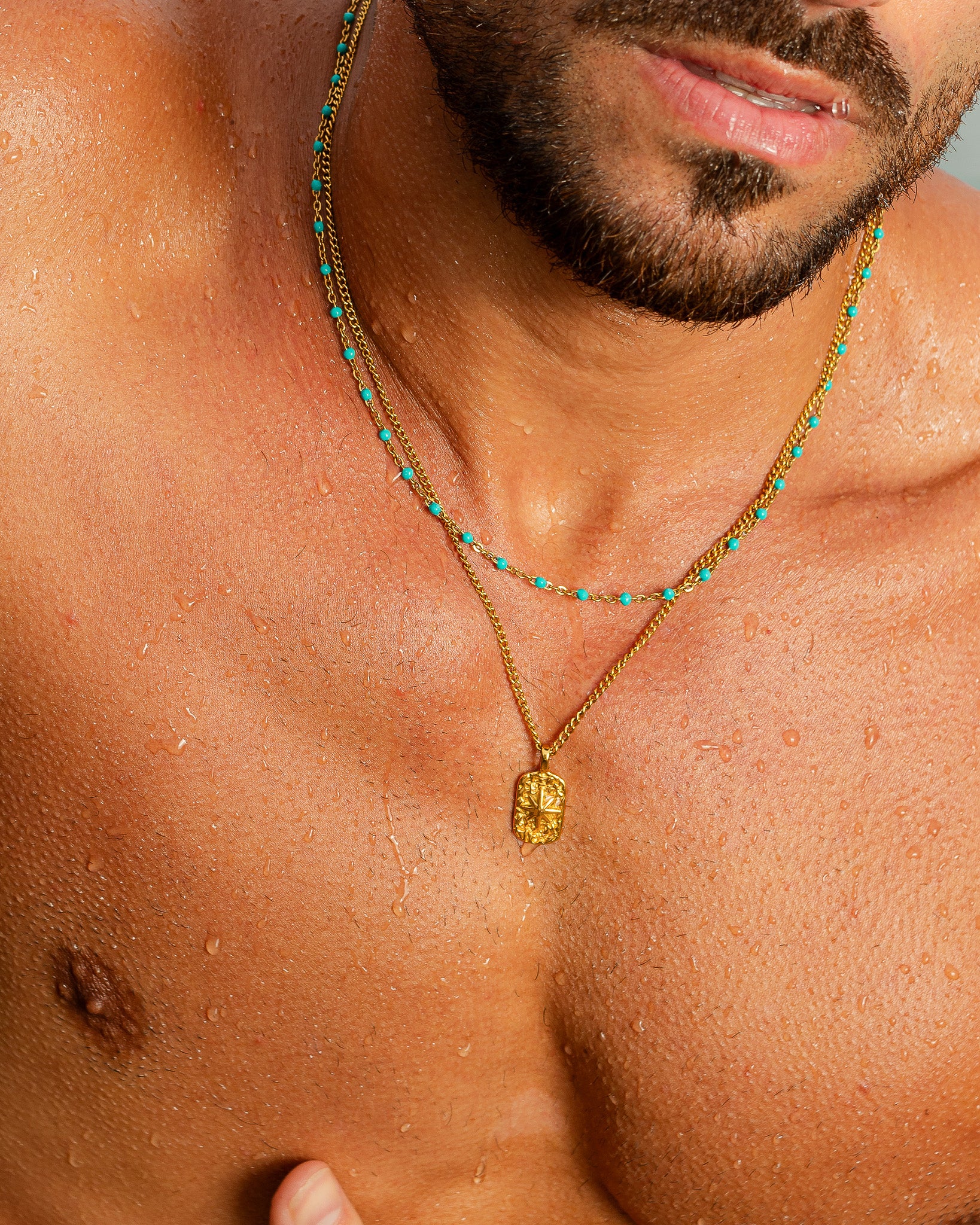 Gold necklace with turquoise beads and a carved rectangular pendant worn on the chest