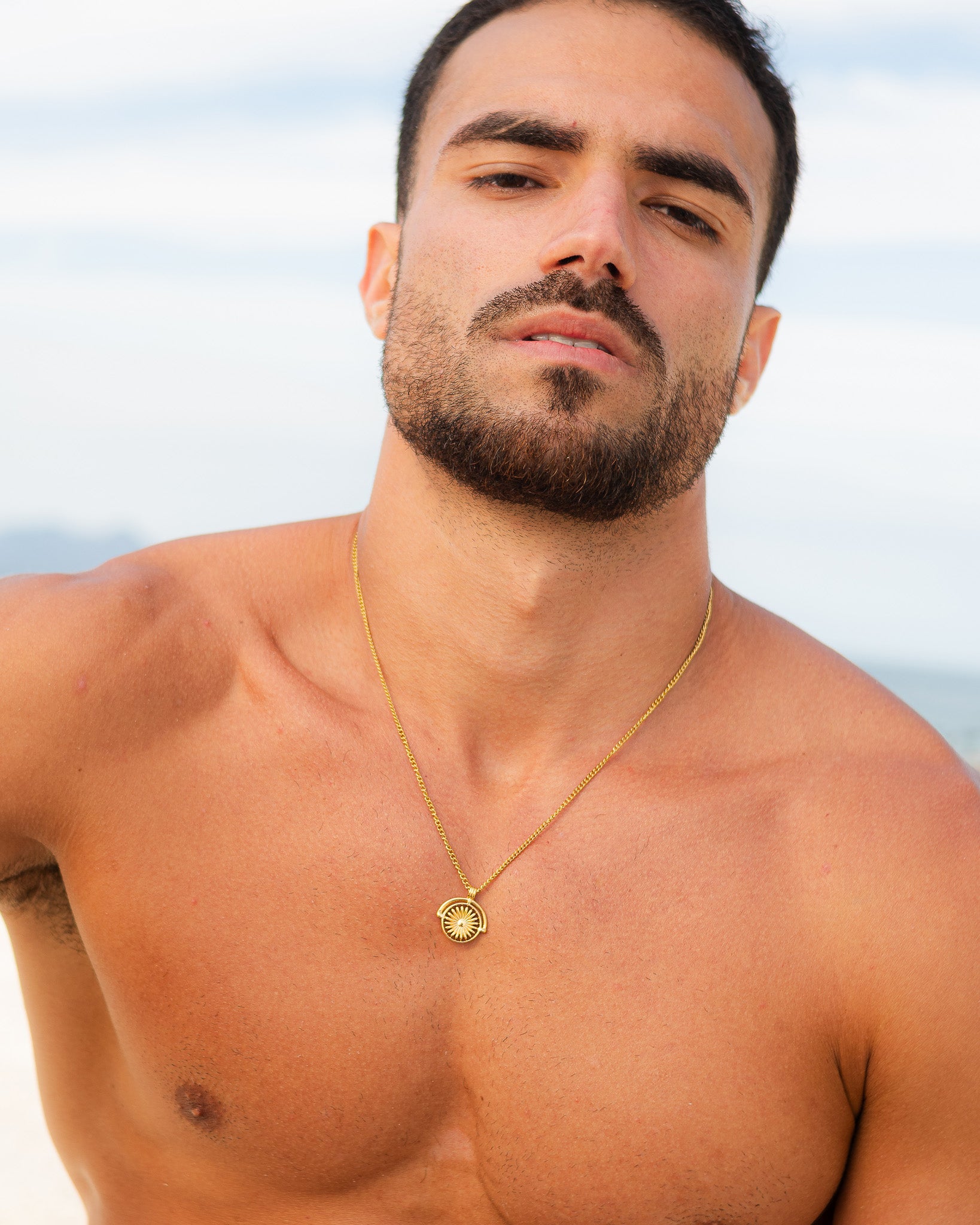 SIRA gold necklace with circular sunburst pendant hanging on a man's chest