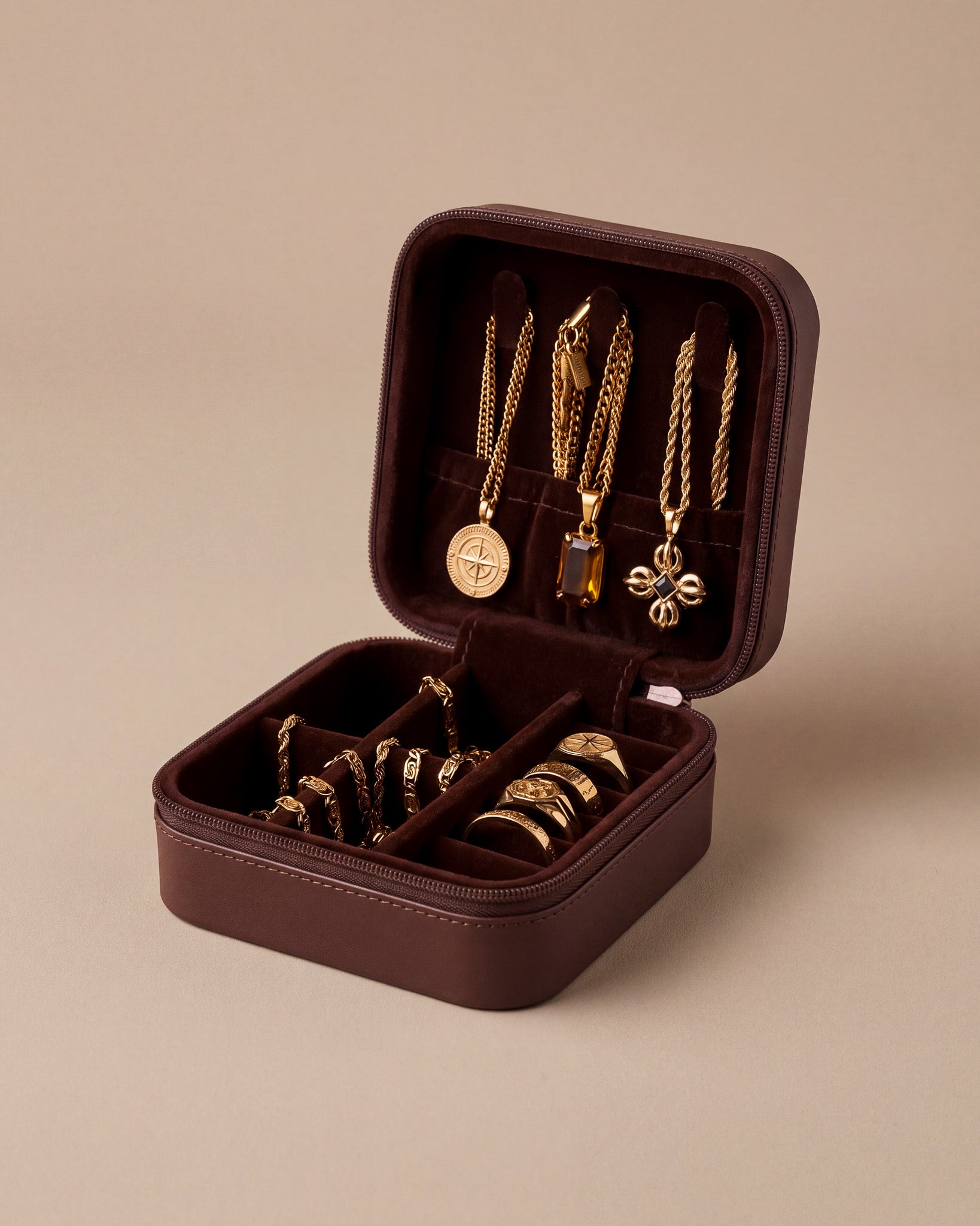 Open burgundy travel jewelry box displaying gold chains and pendants